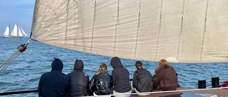 Jugendliche sitzen auf einem Segelschiff und beobachten ein anderes.