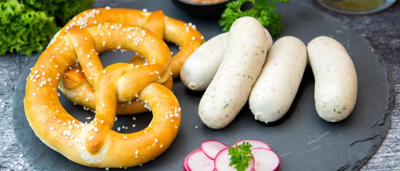 Ein Teller mit einer Brezel und Weißwürsten.
