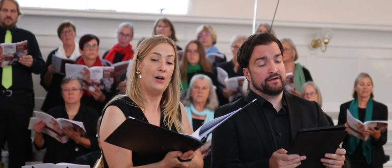 Zwei Musiker singen vor einem Chor und Instrumentalisten.